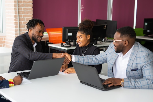 equipe de jovens africanos no escritório trabalhando na mesa com um laptop com um aperto de mão