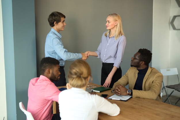 equipe de jovens bonitos no escritório com um aperto de mão