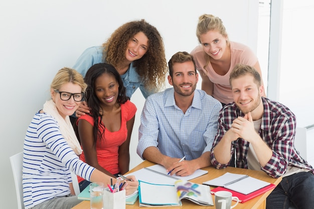 Equipe de jovens designers felizes tendo uma reunião sorrindo para a câmera