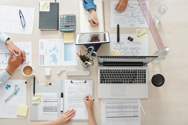 Equipe de marketing trabalhando no projeto à mesa com gráficos, documentos e dispositivos, vista de cima