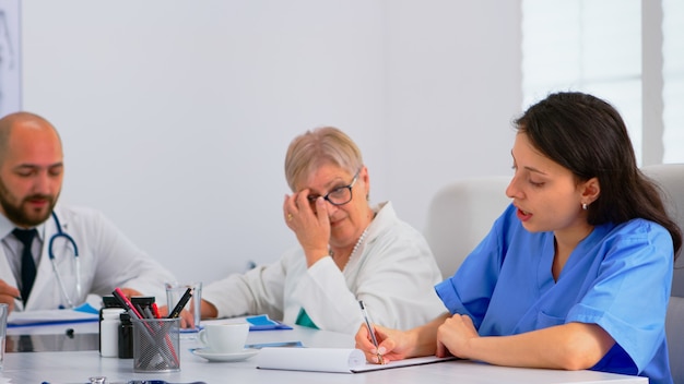 Equipe de médicos em conferência médica, dividindo suas tarefas, discutindo sobre os problemas dos pacientes sentados à mesa no escritório de reuniões do hospital. grupo de médicos falando sobre sintomas de doenças