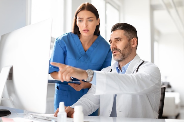 Foto equipe de médicos masculinos e femininos discutindo dados de diagnóstico do paciente usando computador na clínica de escritório trabalhando juntos