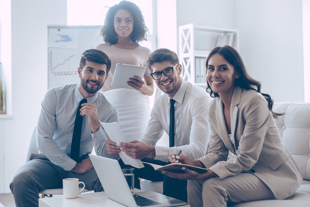 Equipe de negócios alegre. Grupo de quatro jovens olhando para a câmera com um sorriso enquanto estão sentados no sofá do escritório