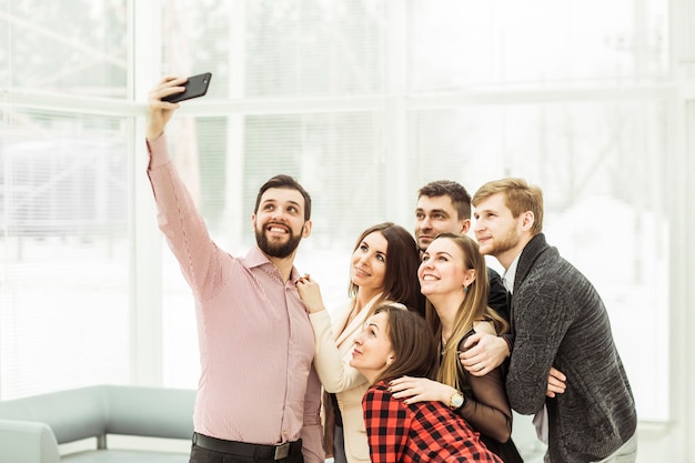 Equipe de negócios amigável tomando uma selfie em pé perto da janela no escritório