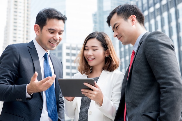 Equipe de negócios asiáticos discutindo e compartilhando o trabalho on-line no computador tablet ao ar livre