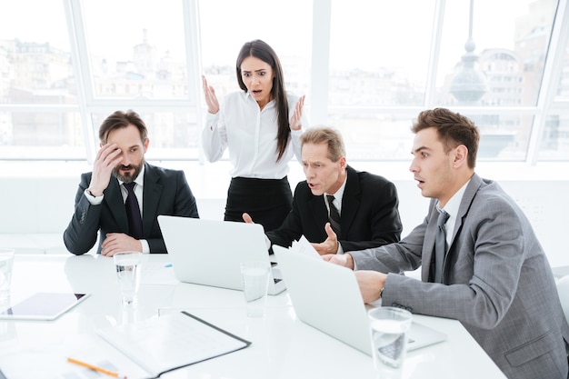 Equipe de negócios chocada perto da mesa olhando para o laptop na sala de conferências