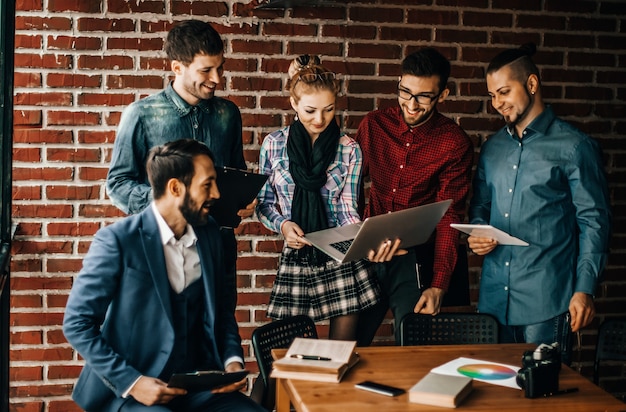 Equipe de negócios com laptop e documentos discutindo um novo projeto perto do local de trabalho em um escritório moderno