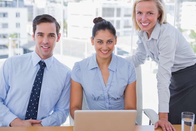 Equipe de negócios com laptop sorrindo para a câmera