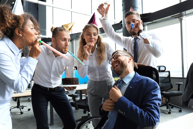 Equipe de negócios comemorando o aniversário de um colega no escritório moderno.