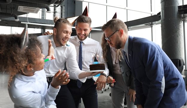 Equipe de negócios comemorando o aniversário de um colega no escritório moderno.