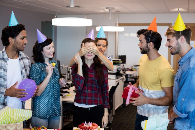 Equipe de negócios criativos fazendo uma surpresa para a faculdade no aniversário dela no escritório