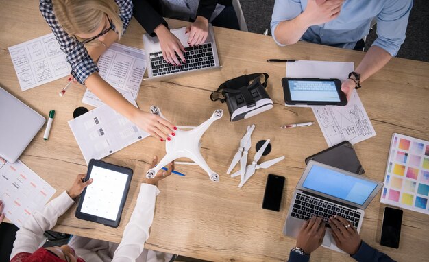 equipe de negócios de inicialização multiétnica discutindo novo plano de negócios, trabalhando em laptop e tablet enquanto aprende sobre a tecnologia de drones para futuros empreendimentos comerciais vista superior