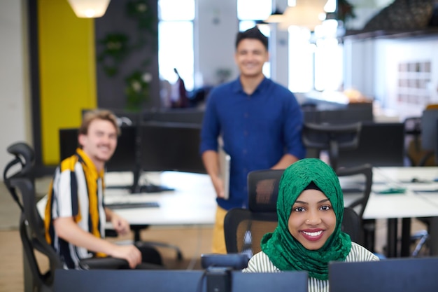 Equipe de negócios de inicialização multiétnica Mulher árabe vestindo um hijab na reunião no brainstorming interior do escritório de plano aberto moderno, trabalhando em laptop e computador desktop