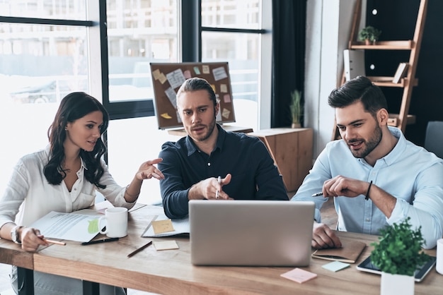 Equipe de negócios de sucesso. grupo de jovens modernos em roupas casuais inteligentes apontando para o laptop