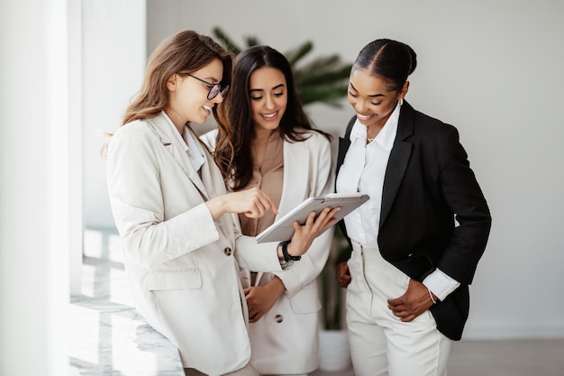 Equipe de negócios feliz de colaboração eficiente de três colegas de trabalho diversos usando tablet digital e