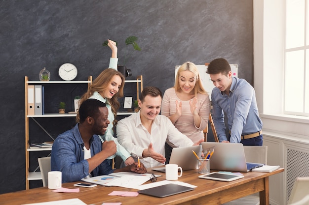 Equipe de negócios jovem aproveitando o sucesso, olhando para a tela do computador, celebrando um projeto bem-sucedido, negociando um contrato, ganhando concurso, copiando espaço