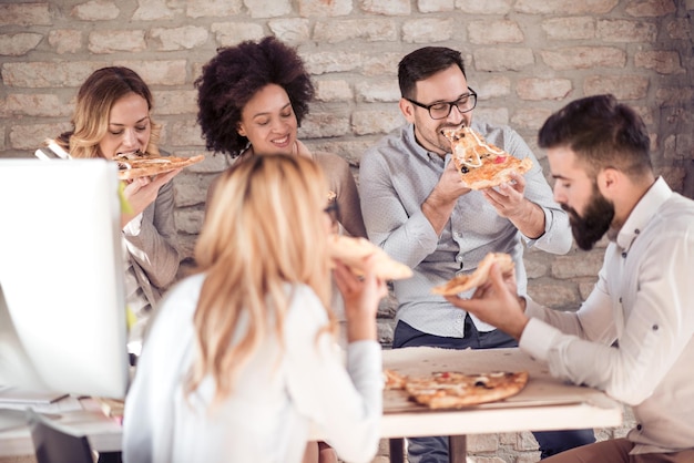 Equipe de negócios jovem feliz comendo pizza no escritório