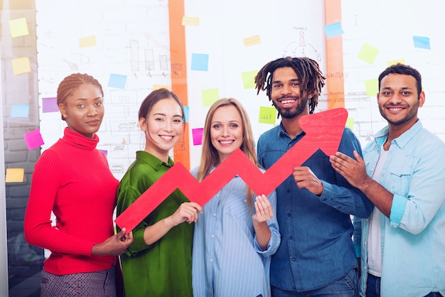 Equipe de negócios jovem, feliz e colorida, segura uma seta vermelha estatística. Conceito de crescimento, sucesso e lucro