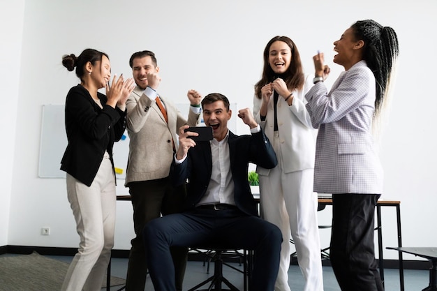 Equipe de negócios jubilosa olhando para a tela do smartphone