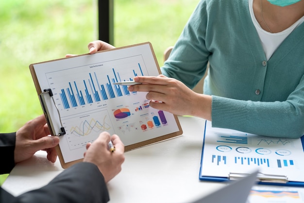 Equipe de negócios segurando um gráfico apontando para o trabalho de contabilidade estatística de apresentações de gráfico na reunião.