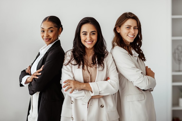 Equipe de negócios três diversas colegas do sexo feminino em trajes formais em pé com os braços cruzados no escritório