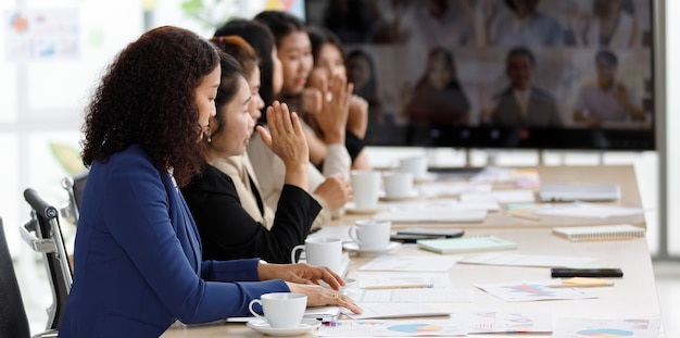 Equipe de oficial de mulher de negócios bem-sucedida asiática de meia idade em roupas de negócios formais, sentado na sala de reuniões de videoconferência, olhando para documentos de papelada de diagrama de gráfico gráfico na mesa.