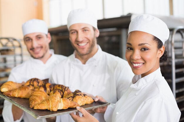 Equipe de padeiros sorrindo na câmera com bandejas de croissants