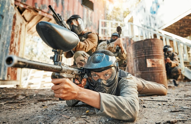 Equipe de paintball e pessoas em ação com arma para competição de torneio e batalha na natureza Esportes militares e homens no chão atirando na arena ao ar livre para treinamento de jogos de aventura ou desafio