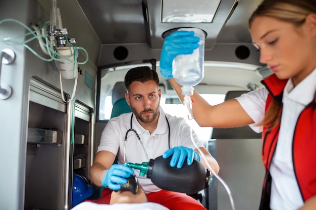 Equipe de paramédicos do EMS fornece ajuda médica ao paciente ferido a caminho do hospital assistente de atendimento de emergência usando uma máscara de ventilação não invasiva em uma ambulância