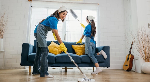 Foto equipe de serviço de limpeza duas mulheres com luvas e uniformes limpam diligentemente a sala de estar empoeirada com um esfregão e spray mantêm a higiene e a pureza agência de limpeza de casa pequeno negócio