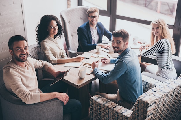 Equipe de sucesso. Jovens alegres olhando para a câmera com um sorriso enquanto estão sentados à mesa do escritório em uma reunião de negócios