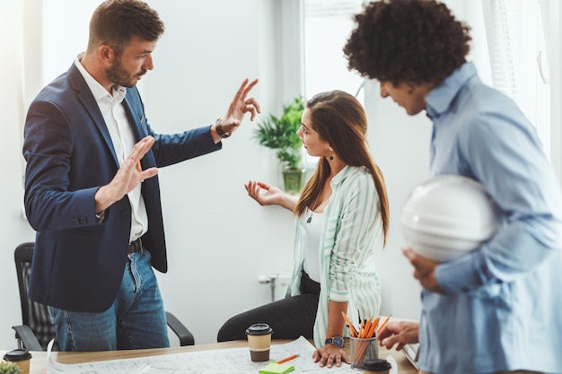 Equipe de três jovens arquitetos trabalhando e se comunicando enquanto analisam plantas de um novo projeto no escritório.