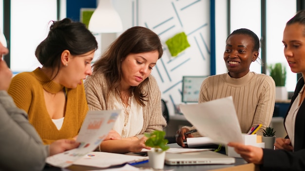 Equipe diversificada de colegas de trabalho profissionais, brainstorming em uma reunião de negócios sob o olhar atento do chefe africano. Empresa de diretor negro avaliando funcionários sentados à mesa discutindo