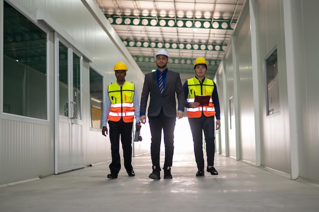 Equipe diversificada de especialistas caminhando pelo projeto de construção de imóveis no local da fábrica com engenheiro civil sênior, arquiteto, trabalhador geral, discutindo detalhes de planejamento e desenvolvimento