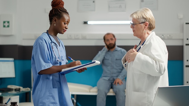 Equipe diversificada de especialistas médicos falando sobre medicamentos para curar doenças e diagnósticos de saúde. Médico e enfermeira afro-americana usando resultados de exames para recuperação de pacientes.