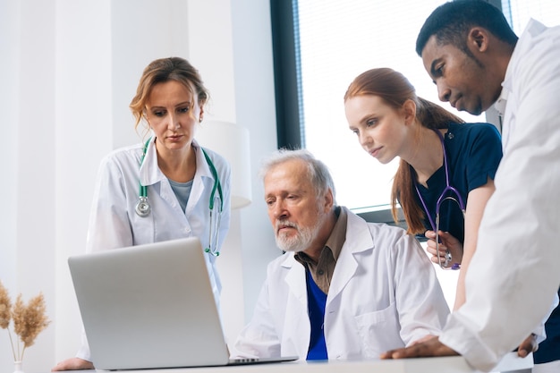 Equipe diversificada de médicos multiétnicas no planejamento de reuniões e brainstorming na sala de reuniões usando laptop em pé no fundo da janela