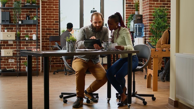 Equipe diversificada de pessoas trabalhando em relatório de negócios no escritório da empresa, analisando informações de gráficos em documentos e tablet. Homem e mulher reunidos para planejar a colaboração na sala de reuniões.