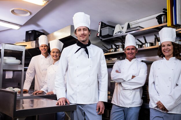 Equipe feliz de cozinheiros juntos em pé na cozinha comercial