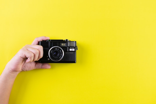 Equipe guardar a câmera do vintage no fundo amarelo com espaço da cópia. Conceito de dia mundial da fotografia.