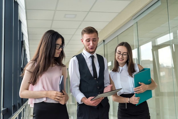 Equipe jovem dos sonhos de três empresários profissionais que discutem a papelada no corredor de um escritório moderno