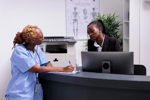 Equipe médica afro-americana analisando formulários de relatório com suporte de seguro de paciente em papéis. Enfermeira e recepcionista trabalhando em consultas de check-up na recepção do hospital, ajuda de saúde.