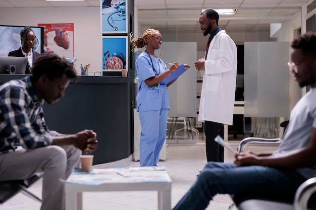 Equipe médica afro-americana falando no lobby, discutindo sobre pacientes e tratamento para curar doenças. Enfermeira e médico conversando sobre saúde na sala de espera.