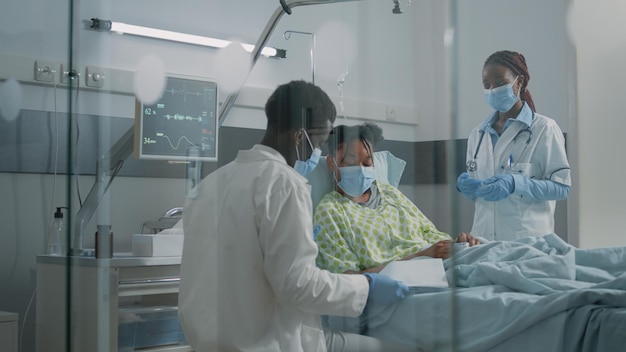 Equipe médica de médicos fazendo consulta com o paciente durante a pandemia na enfermaria do hospital. especialistas e mulheres conversando sobre saúde enquanto usavam máscaras faciais para proteção.