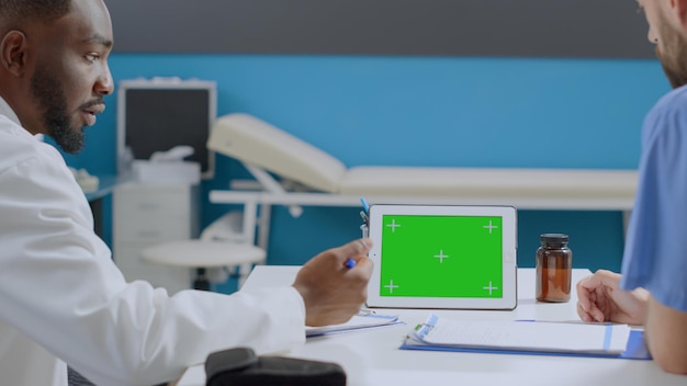 Equipe médica multiétnica discutindo o tratamento medicamentoso, analisando a experiência da doença, trabalhando no escritório do hospital. Computador tablet horizontal de chroma key de tela verde com tela isolada