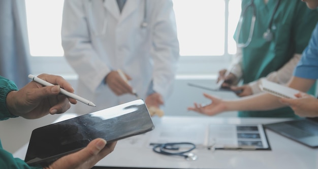 Equipe médica multirracial tendo uma reunião com médicos em jalecos brancos e aventais cirúrgicos sentados em uma mesa discutindo os registros de um paciente