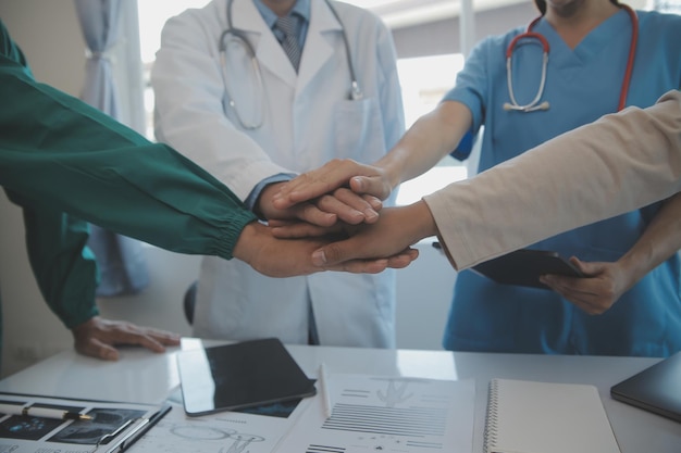 Equipe médica multirracial tendo uma reunião com médicos em jalecos brancos e aventais cirúrgicos sentados em uma mesa discutindo os registros de um paciente