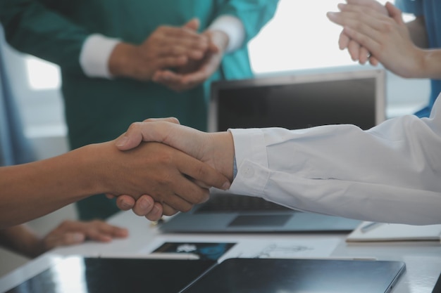 Equipe médica multirracial tendo uma reunião com médicos em jalecos brancos e aventais cirúrgicos sentados em uma mesa discutindo os registros de um paciente