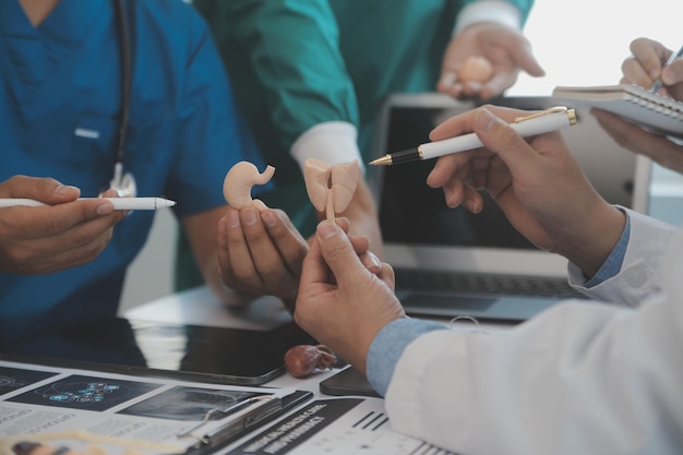 Equipe médica multirracial tendo uma reunião com médicos em jalecos brancos e aventais cirúrgicos sentados em uma mesa discutindo os registros de um paciente