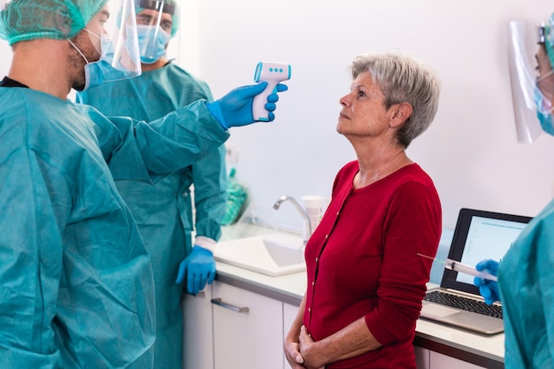 Equipe médica que mede a febre de uma mulher idosa durante um surto de pandemia de coronavírus - Médico e enfermeiro examinam pessoas para a doença Covid 19