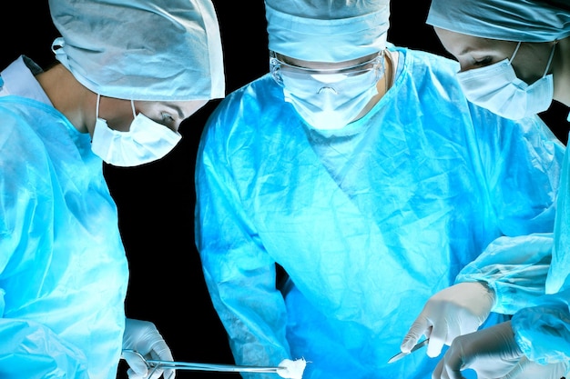 Equipe médica realizando operação. grupo de cirurgião no trabalho na sala de cirurgia em tons de azul.